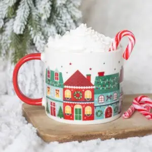 Taza Christmas Street con casitas navideñas y asa roja en una escena festiva con nata y bastones de caramelo